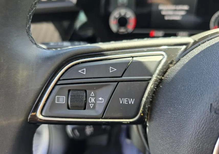 Gros plan sur les commandes gauche du volant cuir de l’Audi A3 Sportback gris argent, boutons de navigation et affichage.