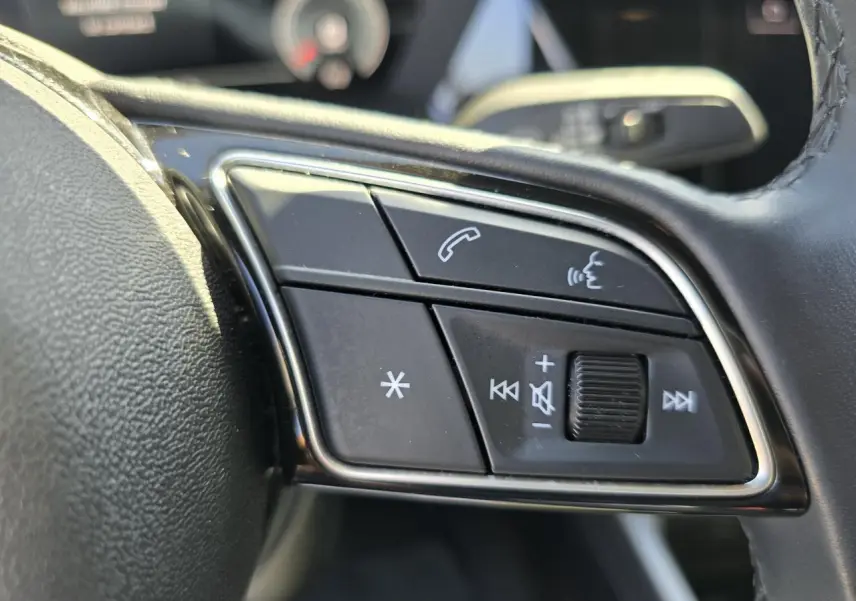Gros plan sur les commandes multifonctions en cuir du volant côté gauche de l'Audi A3 Sportback gris argent Fleuret.