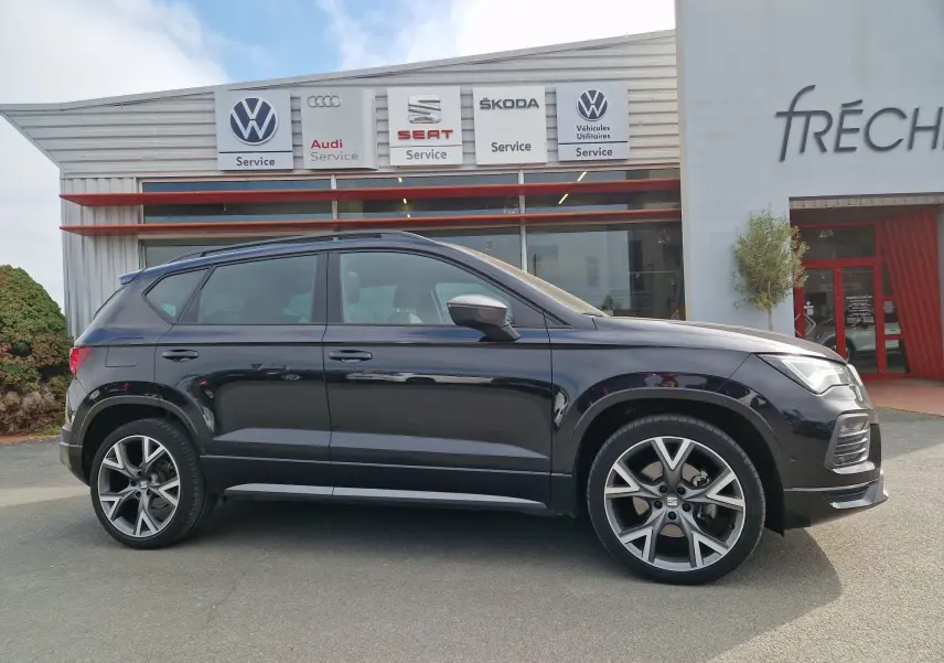 Vue de profil côté gauche d’un SEAT Ateca noir 2023 avec jantes alu 19 pouces, garé devant un service automobile.
