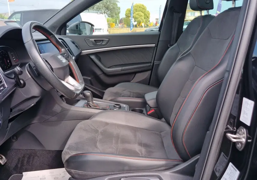 Vue intérieure côté conducteur du SEAT Ateca noir 2023, avec toit panoramique et sièges en cuir noir à surpiqûres rouges.