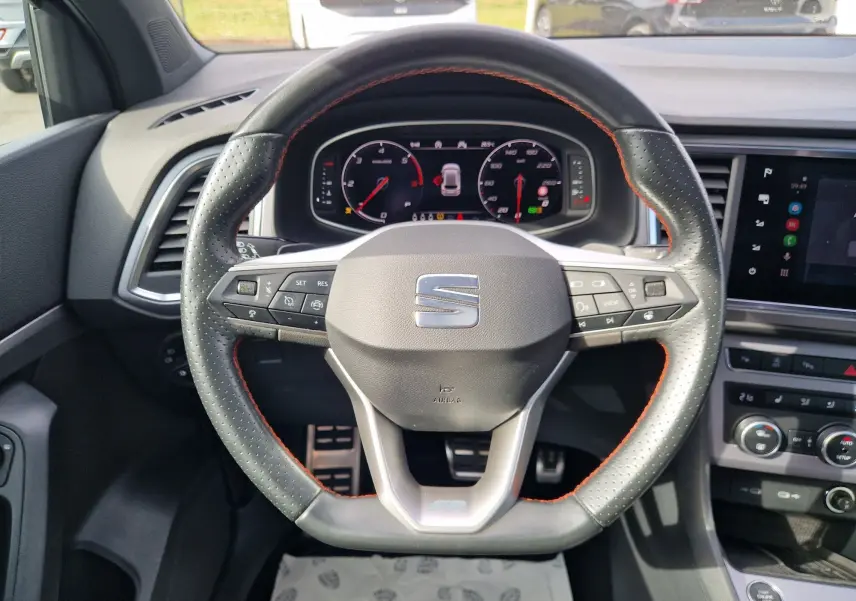 Vue rapprochée du volant perforé avec surpiqûres orange et tableau de bord numérique du SEAT Ateca 2023.