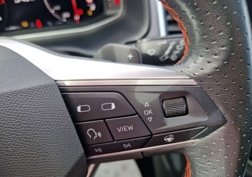 Gros plan sur les commandes à droite du volant en cuir noir perforé avec surpiqûres orange du SEAT Ateca noir 2023.