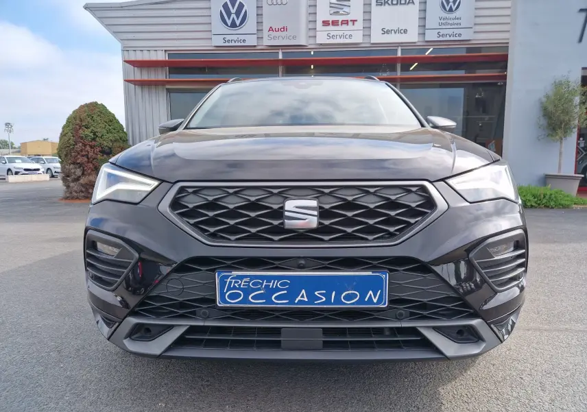 Vue de face d’un SEAT Ateca noir 2023 avec calandre hexagonale et plaques d’immatriculation « Fréchic Occasion » devant un garage multimarques.