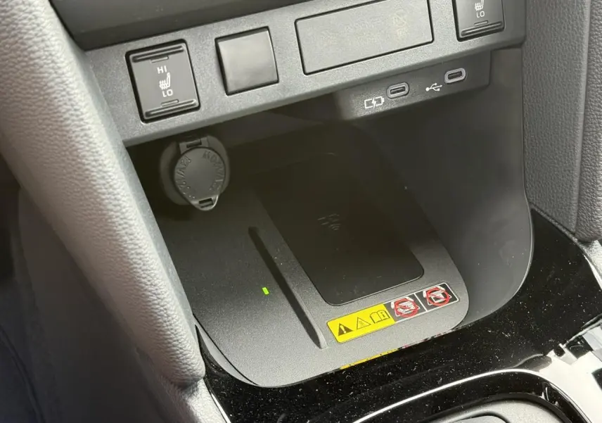 Gros plan sur la console centrale de la Toyota Yaris Cross 2026, montrant le chargeur à induction et commandes sièges chauffants.