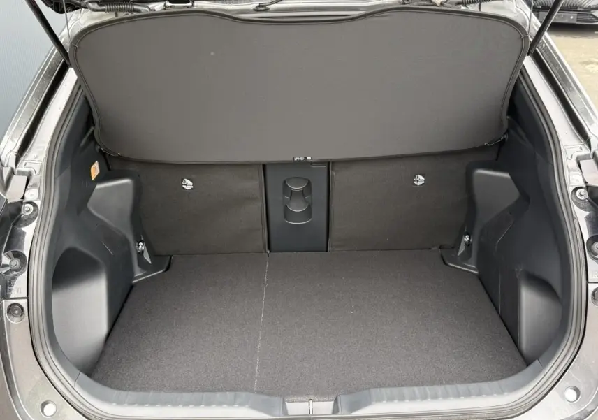 Coffre ouvert vu de l'arrière d'une Toyota Yaris Cross gris Atlas, montrant un plancher plat et un cache-bagages relevé.