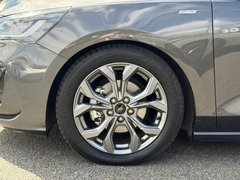 Gros plan sur la roue avant gauche d'une Ford Focus gris lunaire métallisé avec jante alu et badge ST-Line X.