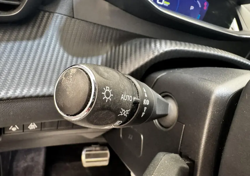Gros plan sur la commande d’éclairage noire à gauche du volant dans l’habitacle du Peugeot E-2008 électrique noir.