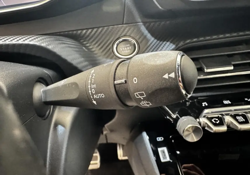 Gros plan sur la commande d’essuie-glace à gauche du volant cuir dans l’habitacle noir du Peugeot E-2008 électrique GT Pack.