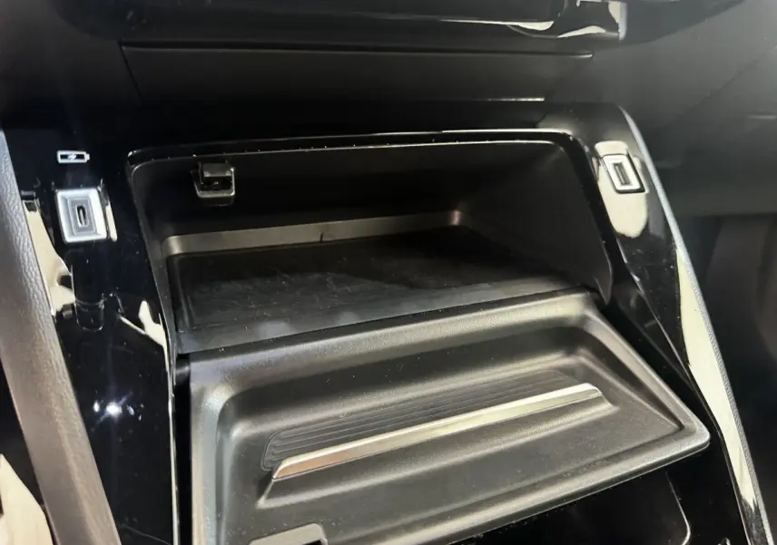 Gros plan sur le rangement central noir brillant du Peugeot E-2008 électrique GT Pack 2021, avec ports USB visibles.