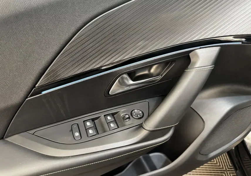 Gros plan sur la porte intérieure côté gauche noire du Peugeot E-2008 électrique GT Pack avec commandes de vitres et poignée cuir.