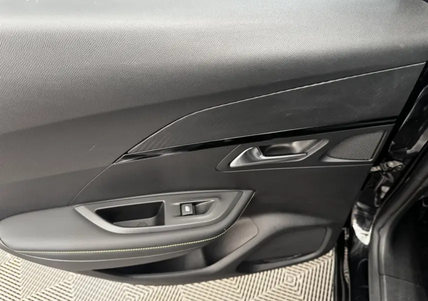 Détail de la porte intérieure côté gauche du Peugeot E-2008 électrique GT Pack noir, avec poignée et bouton de verrouillage.