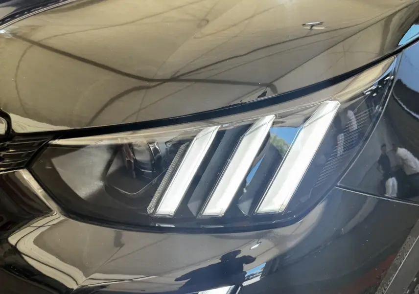 Gros plan sur le phare avant droit noir brillant du Peugeot E-2008 électrique GT Pack 2021 avec signature lumineuse à trois griffes.