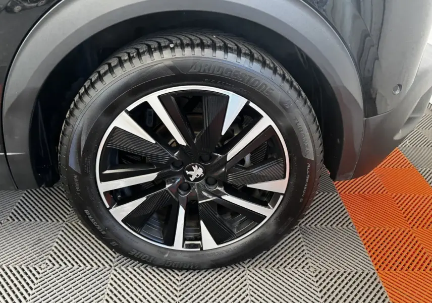 Gros plan sur la roue avant droite noire du Peugeot E-2008 électrique GT Pack avec jante alliage bicolore.