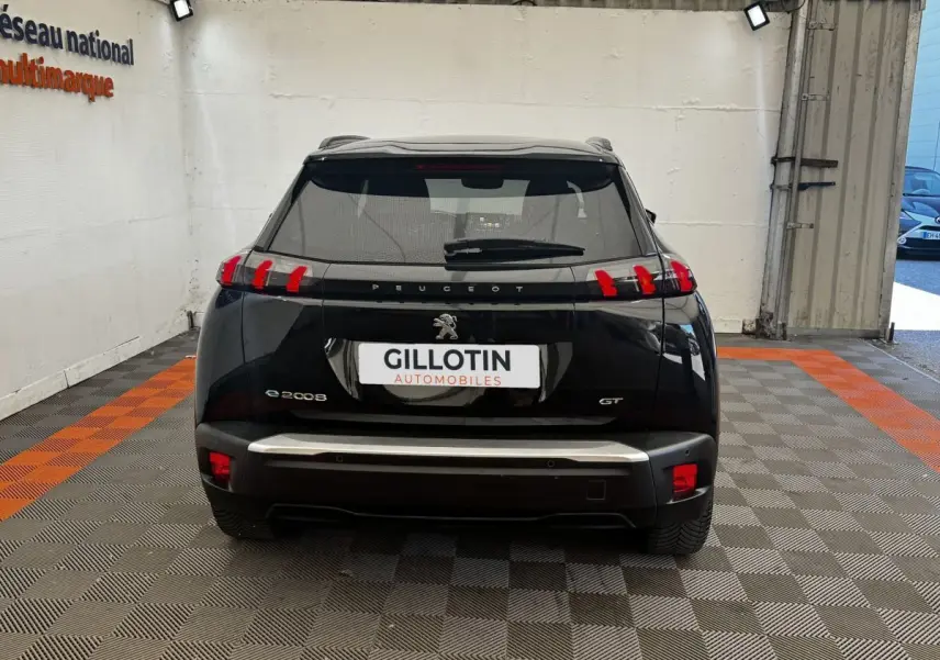 Vue arrière d'un Peugeot E-2008 GT Pack électrique noir, avec feux arrière distinctifs en forme de griffes rouges.