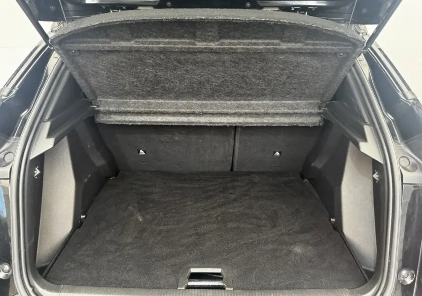 Coffre ouvert vu de l'arrière d'un Peugeot E-2008 électrique GT Pack noir, espace de rangement vide et tapis noir.