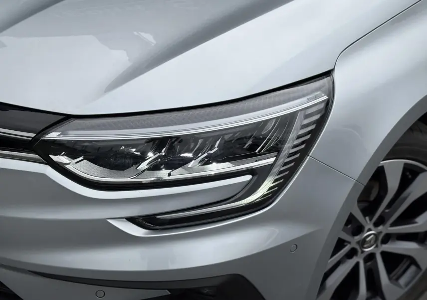 Gros plan sur le phare avant droit et la jante alliage d'une Renault Mégane Break 2024 gris Highland.