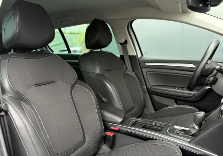 Intérieur avant de la Renault Mégane Break 2024, sièges noirs en similicuir et tissu, console centrale avec levier de vitesses.
