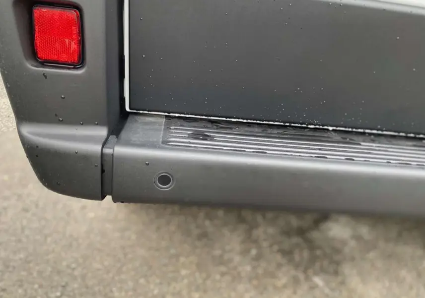 Gros plan sur le pare-chocs arrière gris foncé du Citroën Jumper blanc, avec feu arrière et capteur de recul visible.