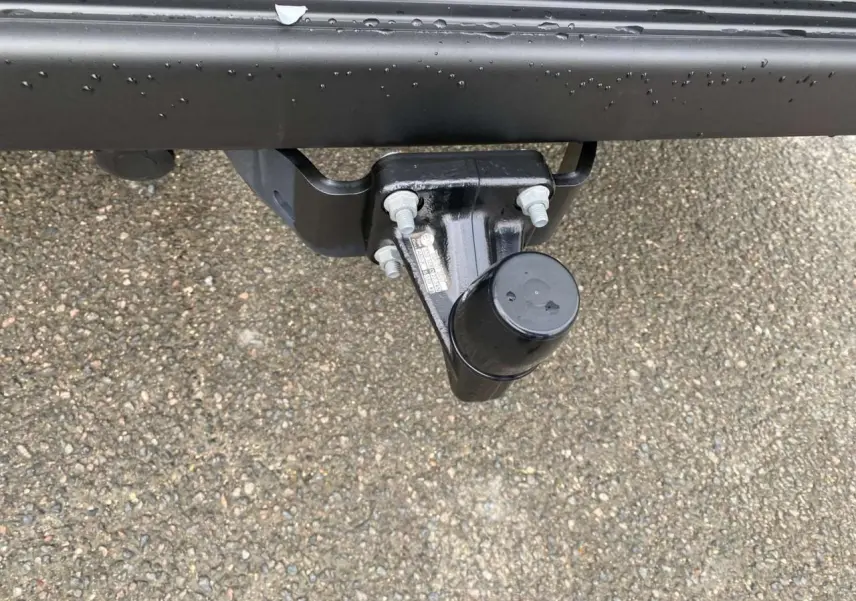 Gros plan sur le crochet d'attelage noir fixé à l'arrière d'un Citroën Jumper blanc, sur sol goudronné humide.