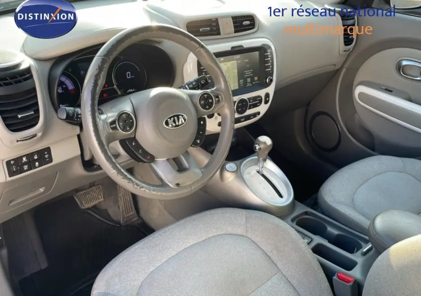 Vue intérieure avant droite du Kia Soul EV 2016, volant multifonction, sièges tissu gris et console centrale argentée.