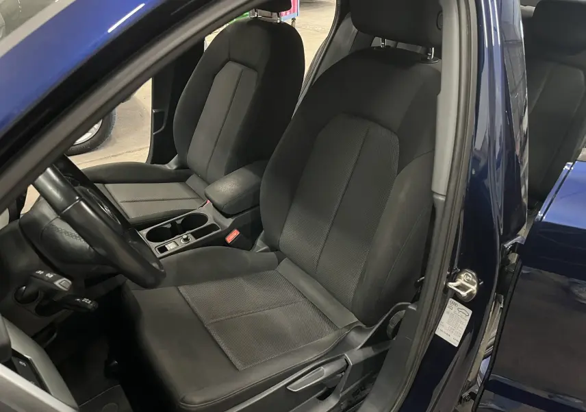 Vue intérieure côté conducteur de l'Audi A3 Sportback bleu métallisé, sièges tissu noir et console centrale visible.