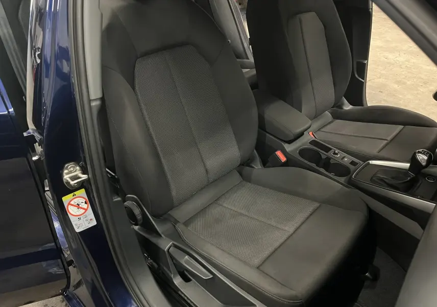 Vue intérieure côté conducteur de l'Audi A3 Sportback bleu métallisé, montrant les sièges noirs et la console centrale avec boîte manuelle.