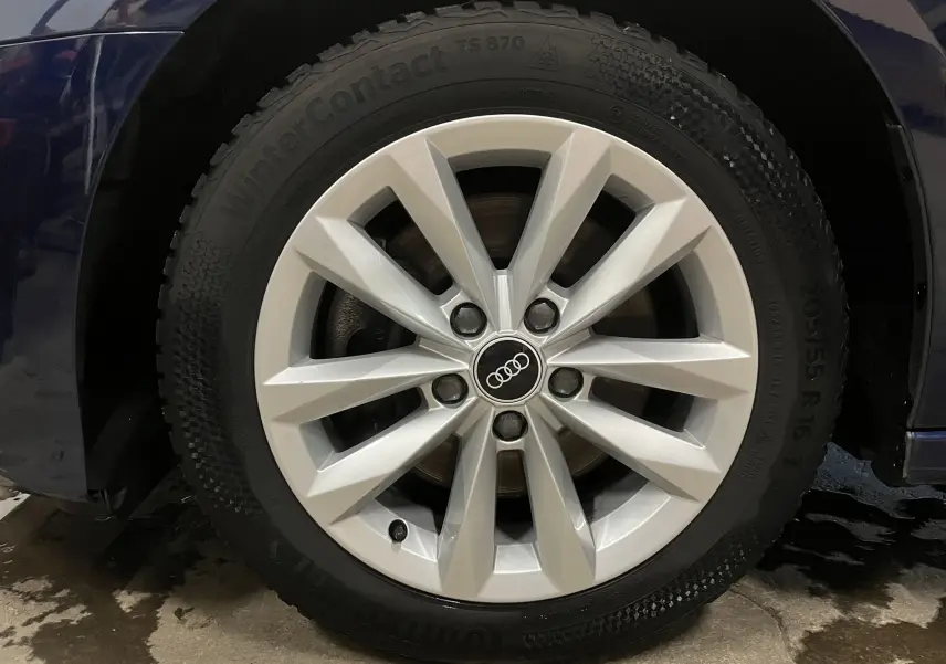 Gros plan sur la roue avant gauche d’une Audi A3 Sportback bleu métallisé avec jante argentée et logo Audi au centre.