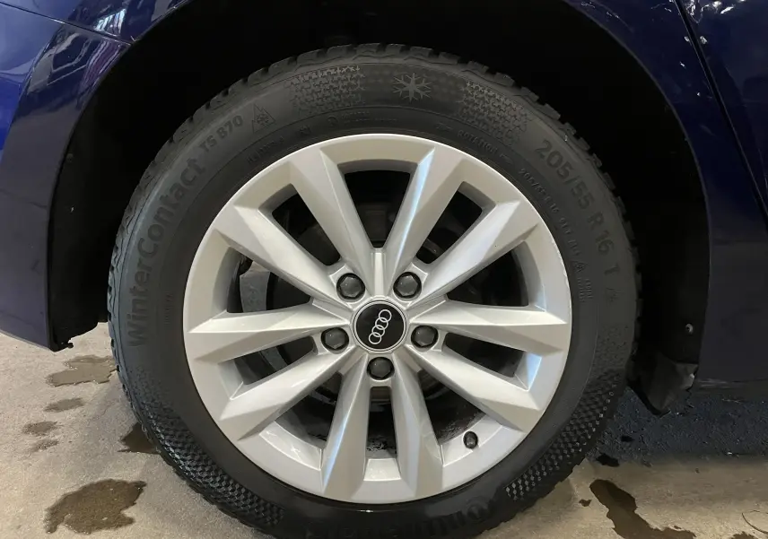 Gros plan sur la roue avant gauche d’une Audi A3 Sportback bleu métallisé avec jante argentée et pneu hiver Continental.