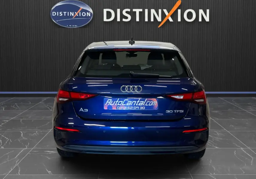 Vue arrière d'une Audi A3 Sportback bleu métallisé 30 TFSI, avec feux arrière allumés dans un showroom.