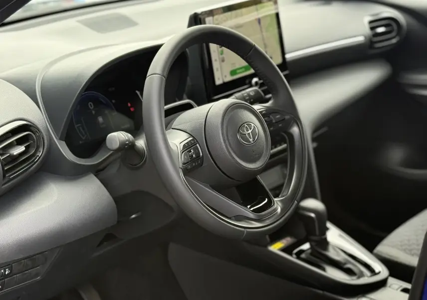 Vue intérieure centrée sur le volant cuir et l’écran tactile du tableau de bord de la Toyota Yaris Cross 2026.