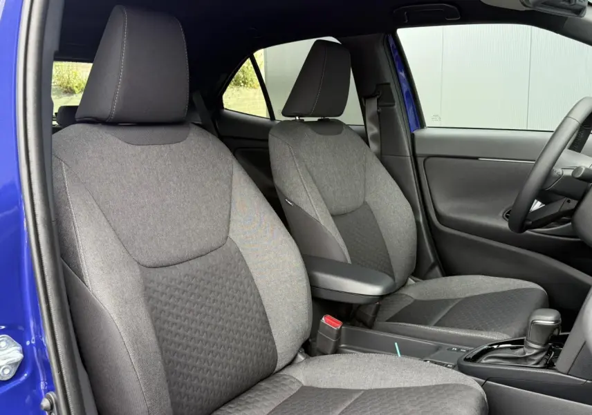 Vue intérieure côté conducteur et passager avant de la Toyota Yaris Cross bleu Genievre, sièges tissu gris et accoudoir central.