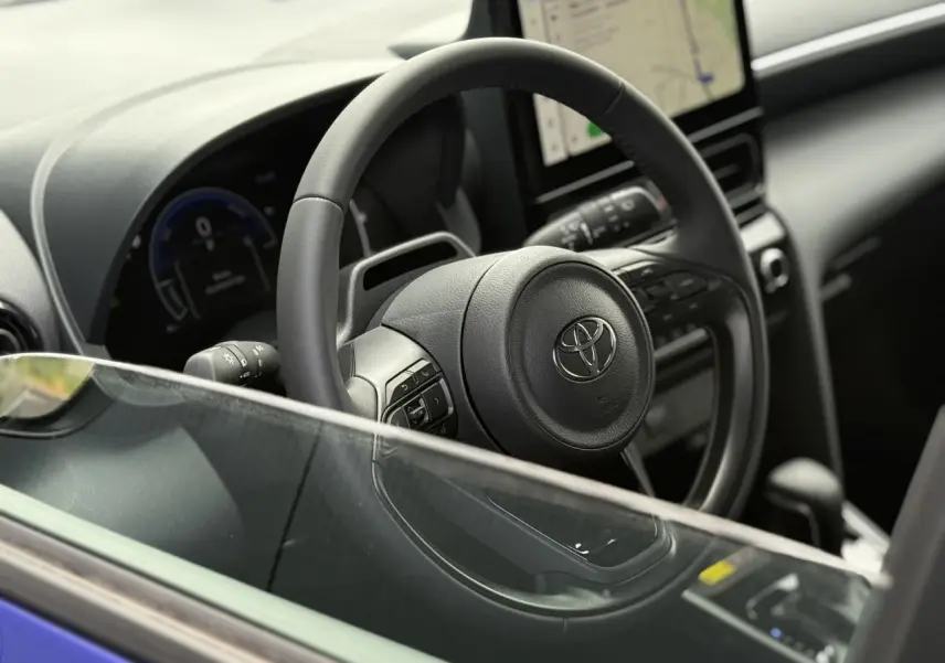 Vue intérieure côté conducteur du Toyota Yaris Cross 2026 bleu Genievre, avec volant cuir et écran tactile central.