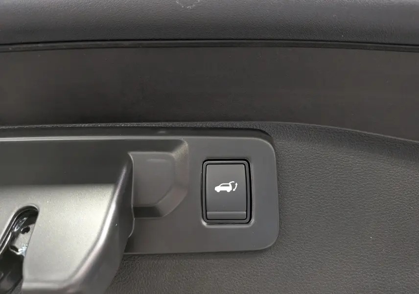 Bouton noir d'ouverture électrique du hayon sur panneau intérieur du coffre du Renault Austral noir.