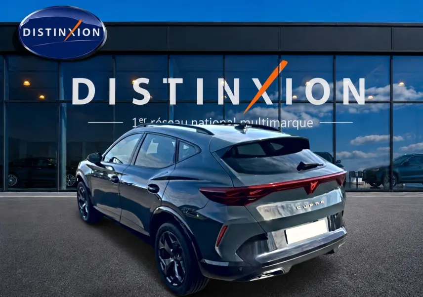 Vue 3/4 arrière droite d'un CUPRA Formentor bleu fjord avec feux arrière LED et jantes noires devant un showroom Distinxion.