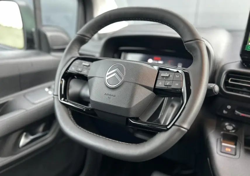 Gros plan sur le volant cuir multifonctions noir du Citroën Berlingo Multispace 2025 avec tableau de bord et commandes visibles.