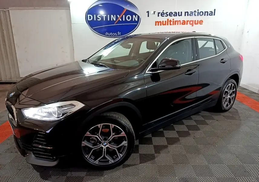 BMW X2 sDrive18i Lounge noir en 3/4 avant droit, avec jantes alliage et phares LED allumés.