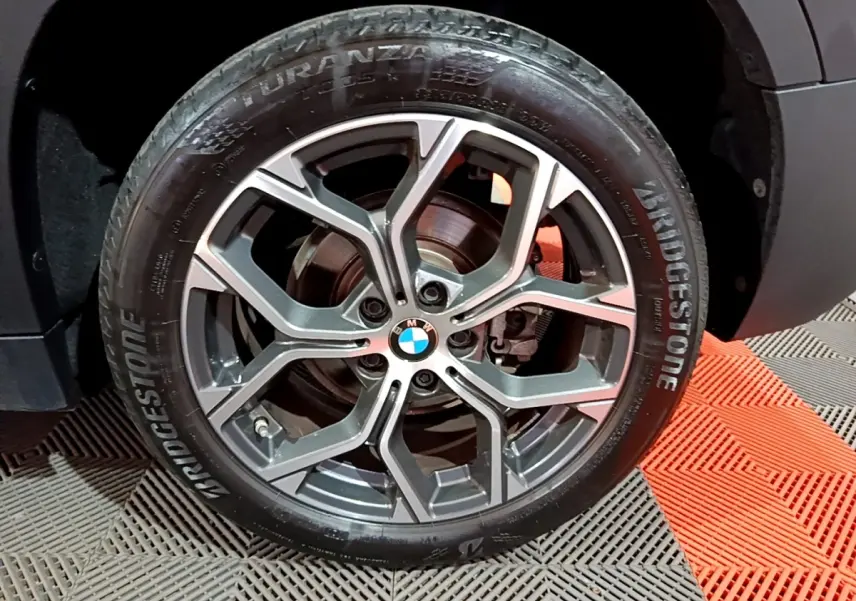 Gros plan sur la roue avant gauche noire d’un BMW X2 sDrive18i Lounge 2023 avec jante alliage et logo BMW central.
