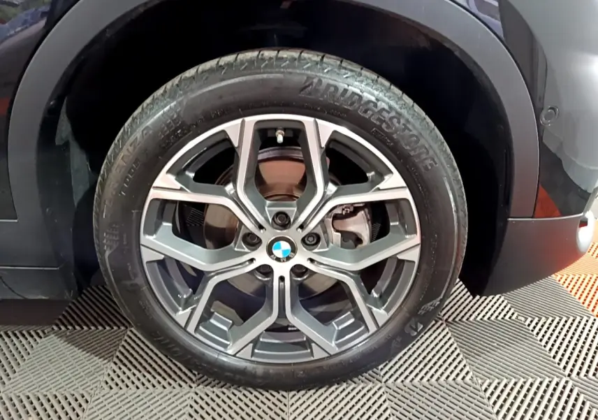 Gros plan sur la roue avant gauche noire d’un BMW X2 sDrive18i Lounge 2023 avec jante alliage distinctive.