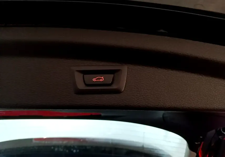 Bouton d'ouverture électrique du coffre visible sur la garniture intérieure du hayon d'un BMW X2 noir.