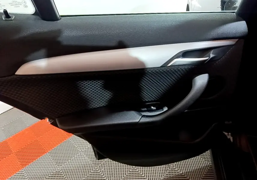 Vue intérieure du panneau de porte côté droit noir avec insert gris clair et commande de lève-vitre sur BMW X2 sDrive18i 2023.