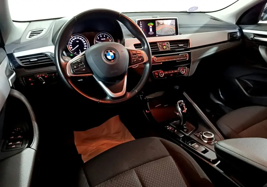 Vue intérieure avant du BMW X2 sDrive18i Lounge 2023, tableau de bord avec écran central et volant cuir multifonctions.