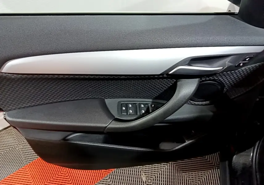 Détail de la porte côté conducteur de la BMW X2 noire 2023 avec commandes des vitres et poignée argentée.