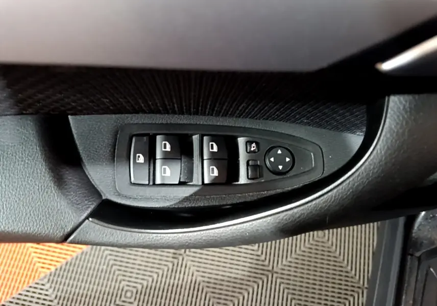 Gros plan sur les commandes de lève-vitres et rétroviseurs côté conducteur d'une BMW X2 noire.