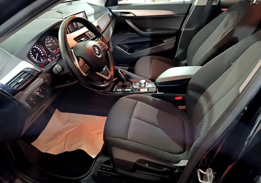 Vue intérieure côté conducteur de la BMW X2 noire 2023, montrant le volant cuir, tableau de bord digital et sièges tissu noirs.