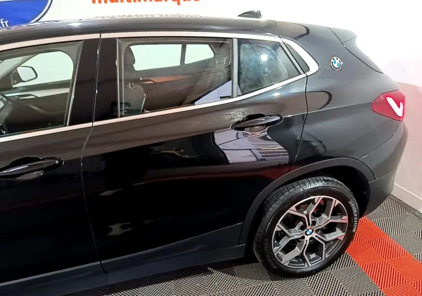 Vue latérale droite d'un BMW X2 noir 2023, mettant en valeur la jante alliage et le logo rond sur l'aile arrière.