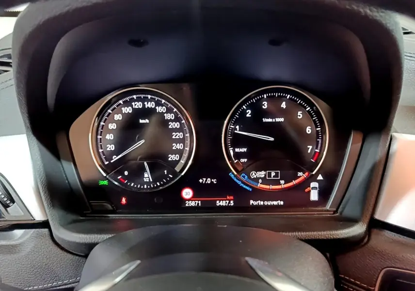 Vue rapprochée du tableau de bord numérique de la BMW X2 sDrive18i 2023, affichant vitesse, compte-tours et alertes.