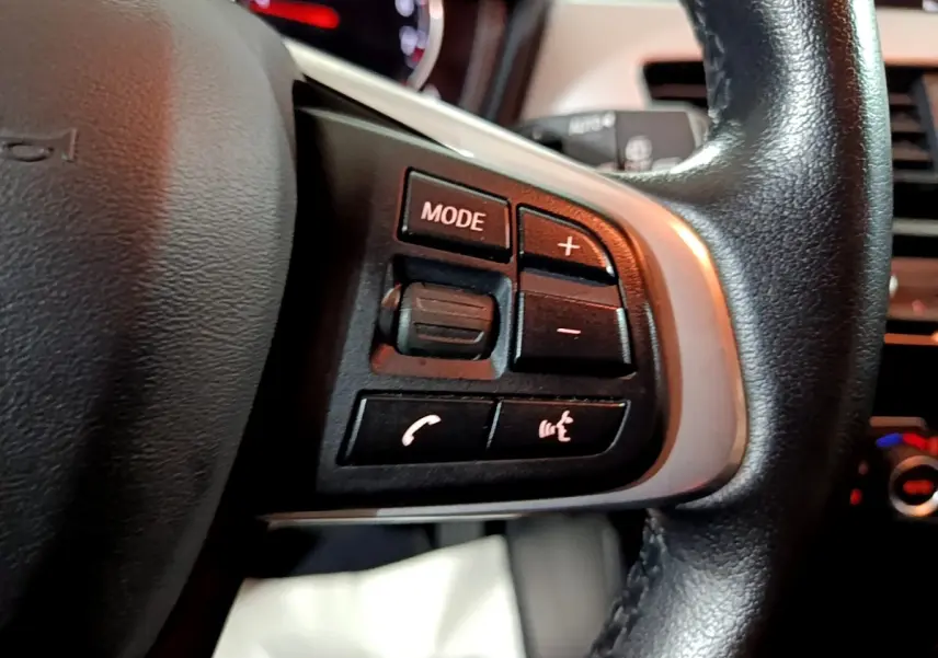 Gros plan sur les commandes gauche du volant cuir noir de la BMW X2 sDrive18i 2023, avec boutons mode et volume.