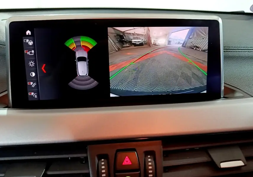 Écran central de la BMW X2 sDrive18i 2023 montrant l’aide au stationnement avec vue caméra arrière et capteurs.