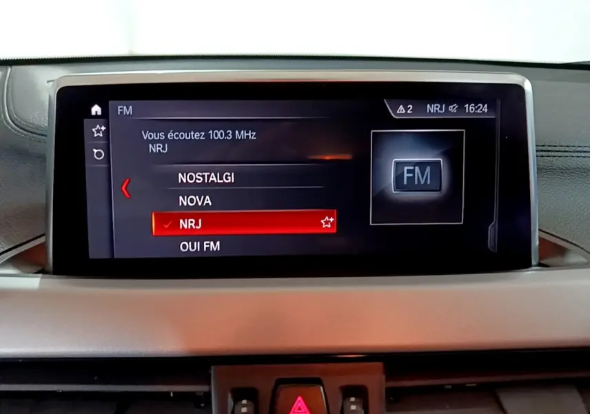Écran central du tableau de bord du BMW X2 sDrive18i Lounge 2023 affichant la sélection radio FM NRJ.