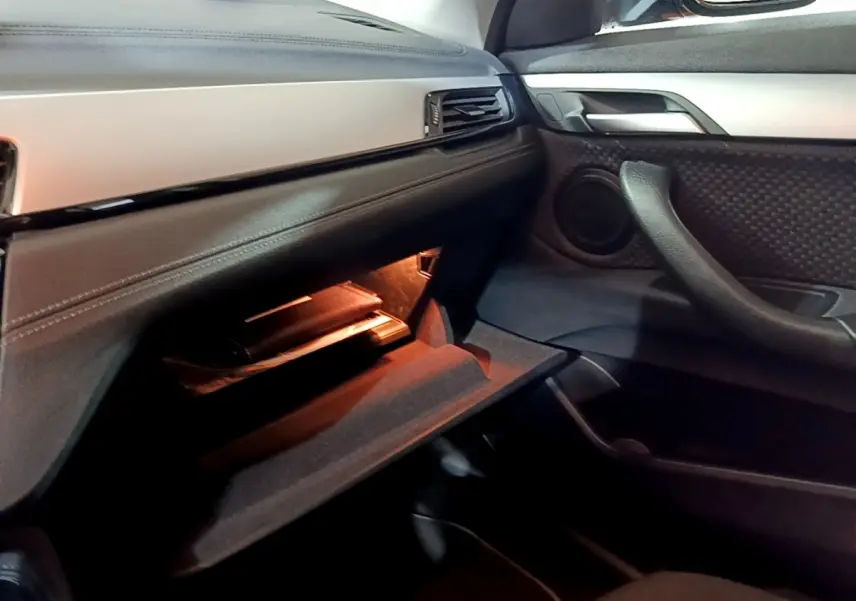 Intérieur BMW X2 sDrive18i 2023 côté passager, boîte à gants ouverte avec éclairage ambiant orange.